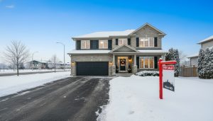 Well-staged Milton Ontario home for sale in winter with snow, warm interior lighting, and a 'For Sale' sign