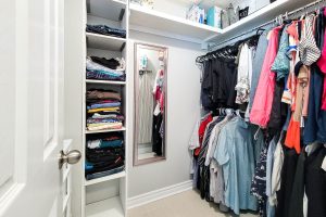 Organized walk-in closet with clothes and mirror.