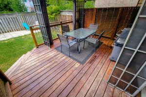 Wooden patio with table, chairs, and grill.