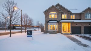 Winter photo of a Milton Ontario house with 'For Sale' sign and cleared walkway, warm interior lights visible