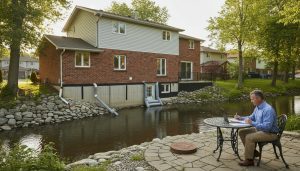 Georgetown home with flood mitigation measures: sump pump discharge, sealed foundation, backwater valve hatch, extended downspouts, homeowner reviewing insurance documents
